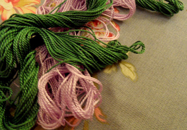 A pile of colorful embroidery floss is resting on a piece of floral fabric. Embroidering may appear difficult, but is easy to master once you know the basic stitches.