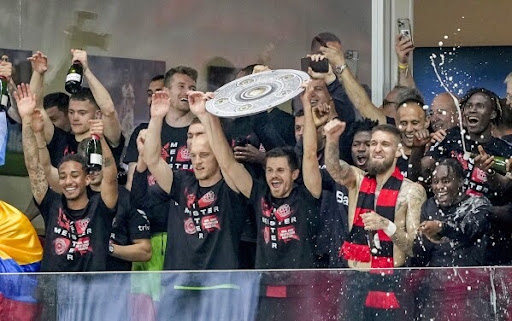 The Bayer Leverkusen team celebrating their title with a cardboard cutout of the Bundesliga trophy.
