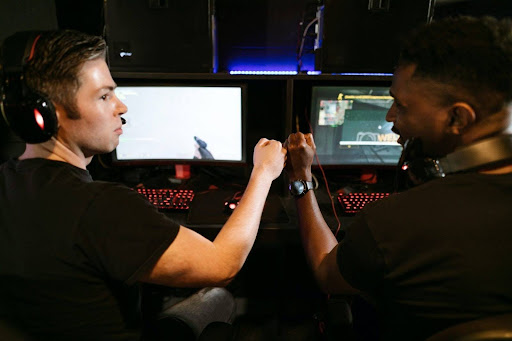 Image of two men fist bumping in front of monitors